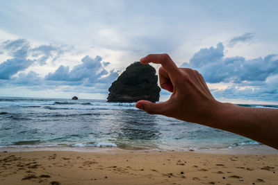 Optical illusion of man holding rock at beach against sky