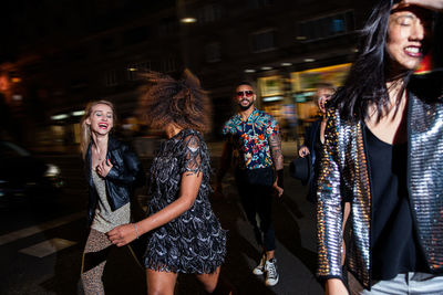 Group of stylish multiracial friends walking together on city street for party at night