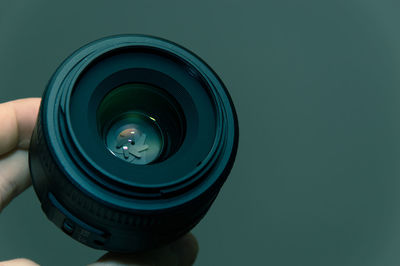 Close-up of cropped hand holding camera lens against green background