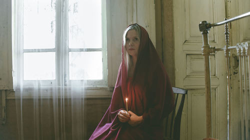 Woman holding candle while sitting on seat at home