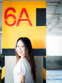 Portrait of smiling young woman standing against number and alphabet on yellow wall