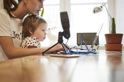 Female influencer sitting with daughter while marketing through laptop at home