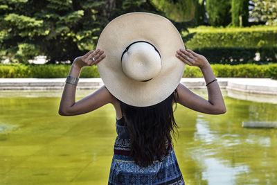 Rear view of woman wearing hat while standing against lake