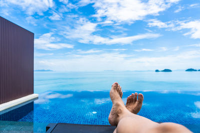 Low section of man relaxing at poolside against blue sky