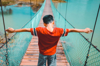 Rear view of boy with arms outstretched standing on footbridge