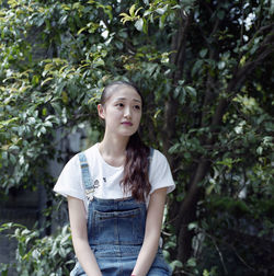 Thoughtful young woman sitting against trees