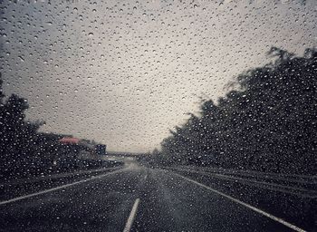 Road against sky seen through car windshield during rainy season