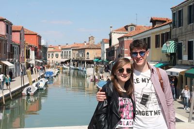 Portrait of couple standing against canal in city during sunny day