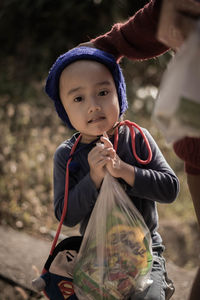 Cropped image of parent with son holding plastic bag while standing on field