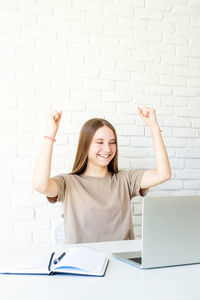 Portrait of smiling young woman using mobile phone against wall