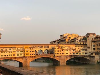 Bridge over river by buildings against sky in city