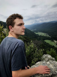 Young man looking away while mountains against sky