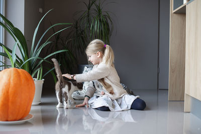 A little girl sits on the floor and holds a cat in her hands