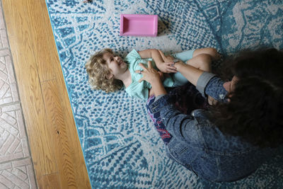 High angle view of happy mother tickling cute daughter on carpet at home