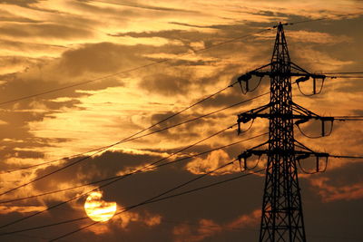 Low angle view of electricity pylon against sky during sunset