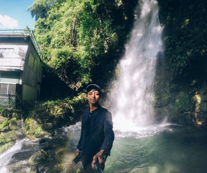 Portrait of young man standing against waterfall