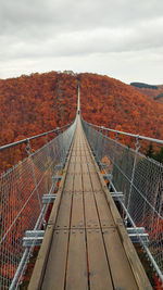 Empty footbridge leading towards mountain against sky