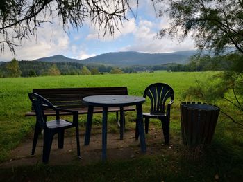 Empty chairs and tables on field against sky