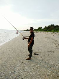 Man fishing at beach against sky