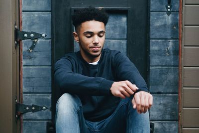 Smiling young man sitting against door