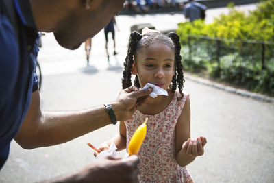 Father cleaning face of daughter with tissue at park