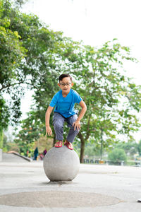 Outdoor portrait of a cute malaysian little boy trying to jump from a concrete ball at the park.