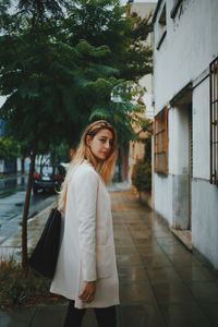 Portrait of young woman standing on sidewalk