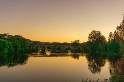 Arch bridge over river against sky during sunset