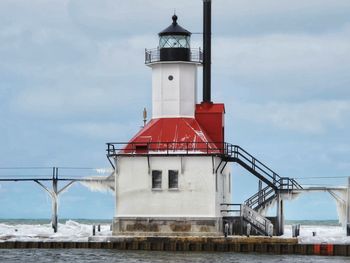 View of lighthouse by building against cloudy sky