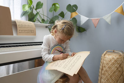 Blond girl writing on musical sheet at home