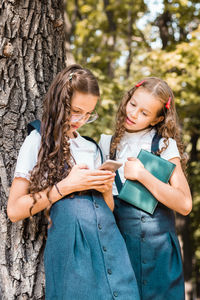 Classmates in school uniform with a book looking at a smartphone day in the park. vertical view