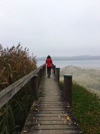 Rear view of woman walking on wooden pier against sea and sky