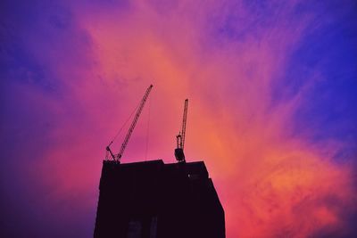 Low angle view of silhouette crane by building against sky during sunset