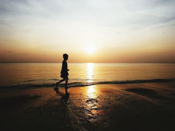 Silhouette man on beach against sky during sunset