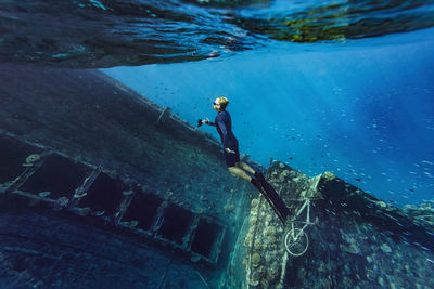 Young man in diving flippers swimming by shipwreck in sea