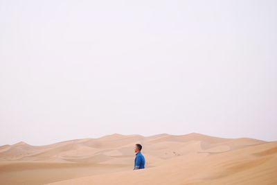 Side view of man amidst sand dunes at desert against clear sky