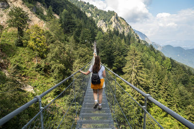 Rear view of woman walking on footbridge leading towards mountain