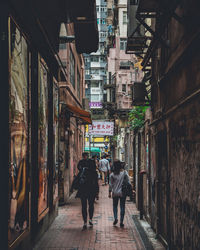Rear view of people walking on street amidst buildings in city