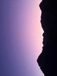 Silhouette rock formation in sea against clear sky