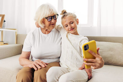 Mother and daughter using mobile phone while sitting on sofa at home