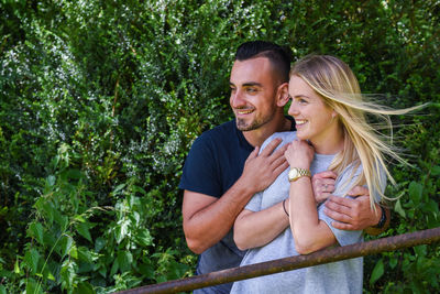 Happy young couple looking away while standing by railing at park