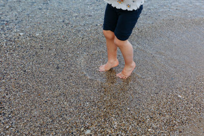 View of barefeet child legs walking on beach in dark pants