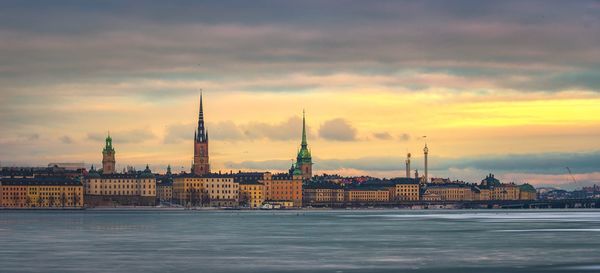 River and buildings against cloudy sky during sunset