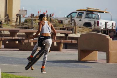 Rear view of young woman with skateboard standing on road in city