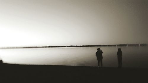 Rear view of silhouette men walking on beach against sky