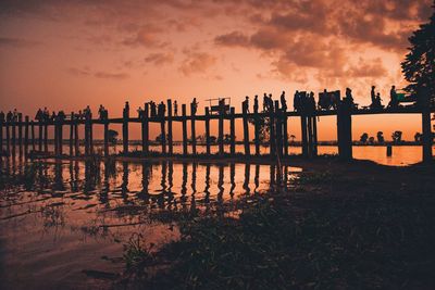 Silhouette wooden posts on beach against sky during sunset