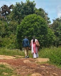 Rear view of mother and son walking on field against trees