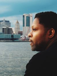 Close-up of thoughtful young man looking away by lake in city