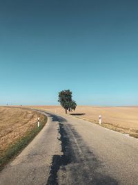 Empty road amidst field against clear sky