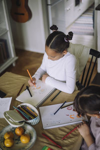 High angle view of female siblings drawing on book while sitting at home